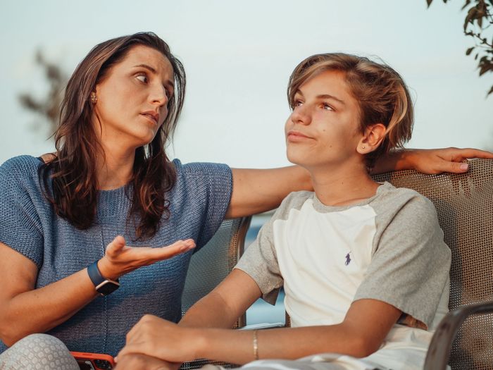 A mother and her teenage son have a serious conversation on a couch
